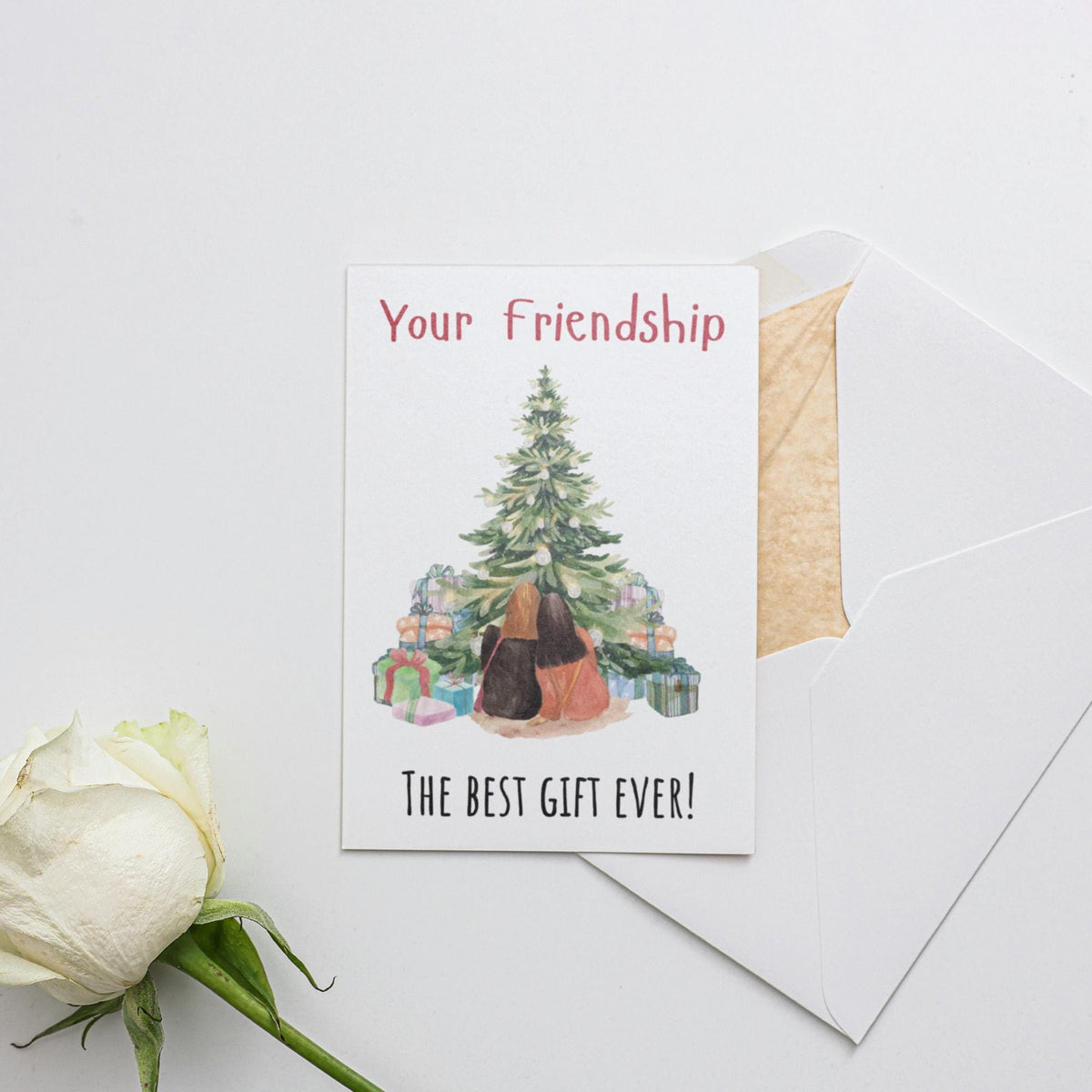 a white rose sitting next to a card with a christmas tree on it